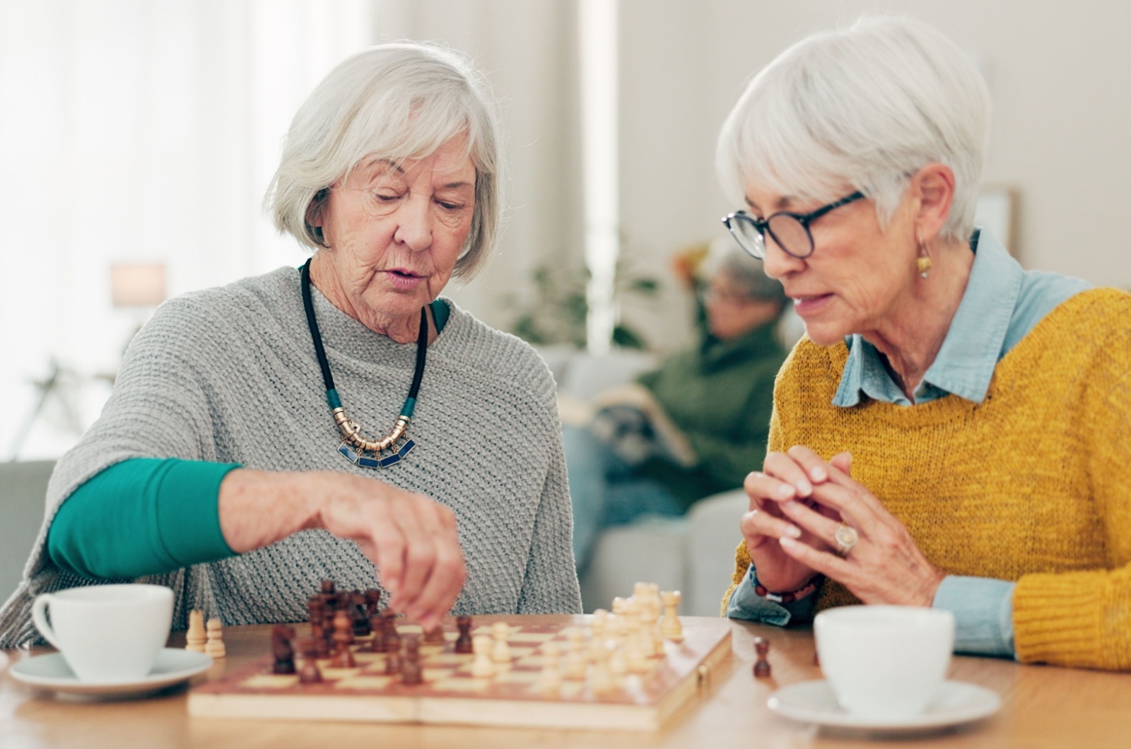 Two senior woman sitting at a table playing chess.