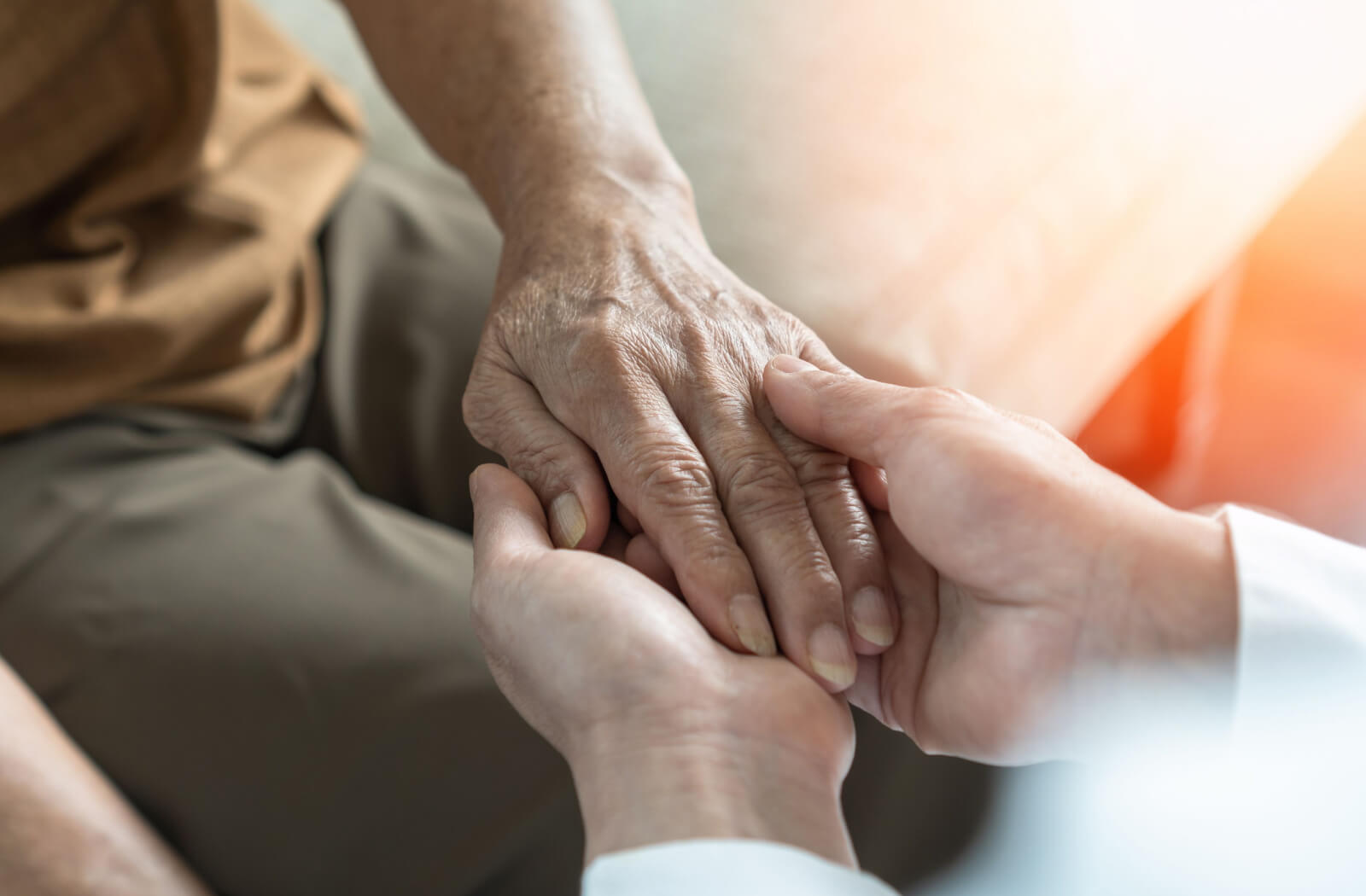 An out-of-frame healthcare professional clasps the hand of an older adult to reassure them after an Alzheimer's diagnosis
