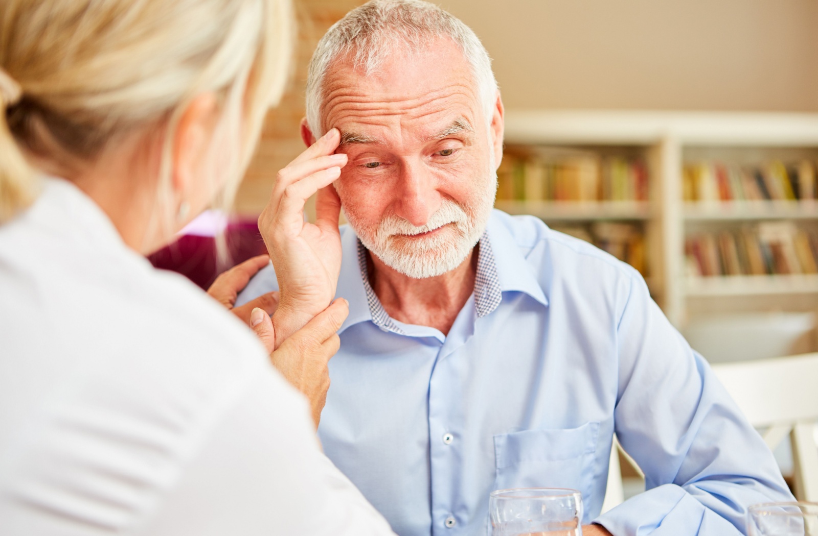 An older adult touches their forehead in confusion during a healthcare checkup for Alzheimer's symptoms with their doctor
