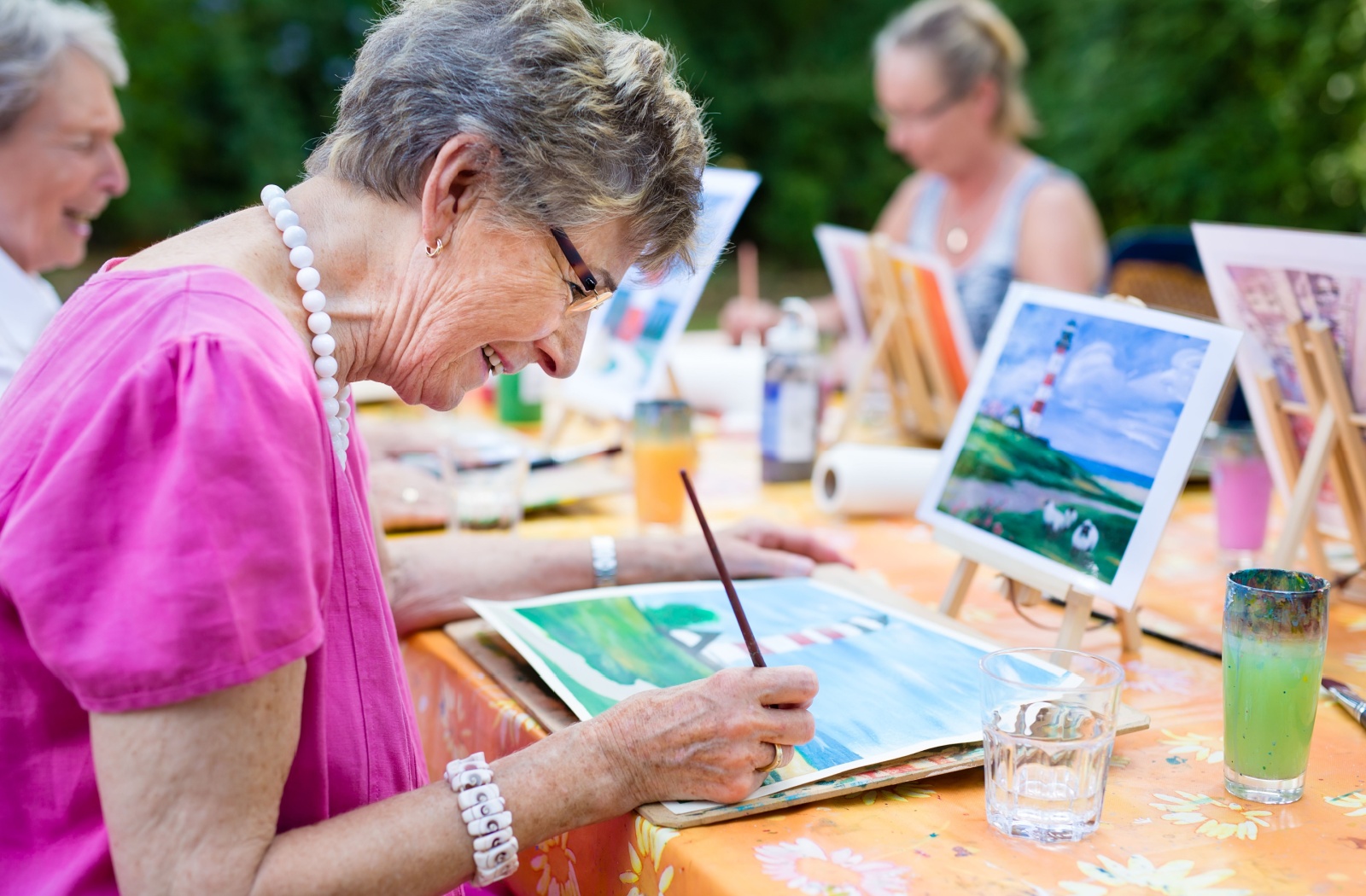 A group of seniors enjoy painting with watercolors while sitting outside.