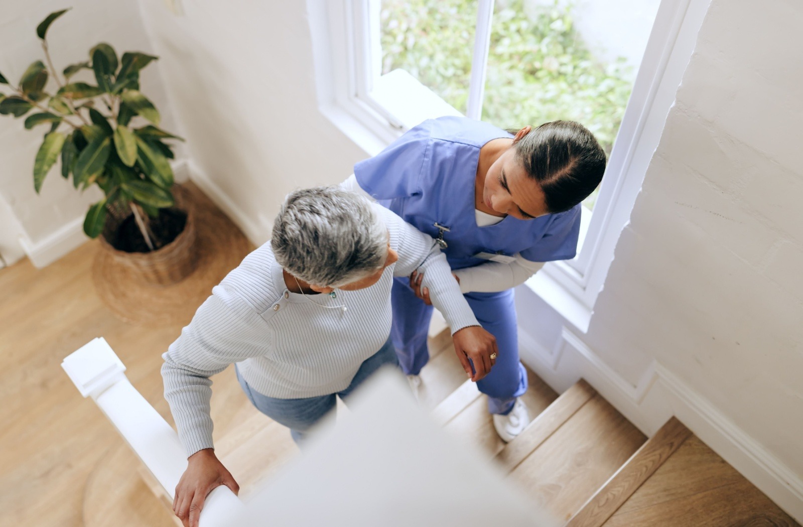 A senior living caregiver assists a resident climbing a flight of stairs.
